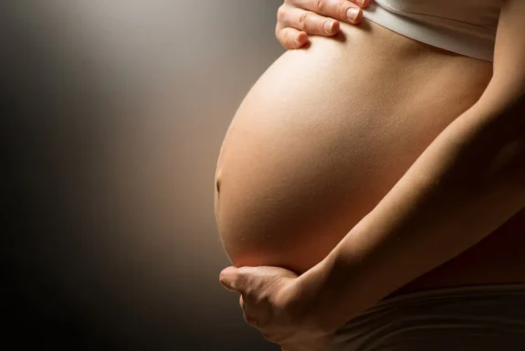 Close-up of a pregnant belly with hands gently resting on it.